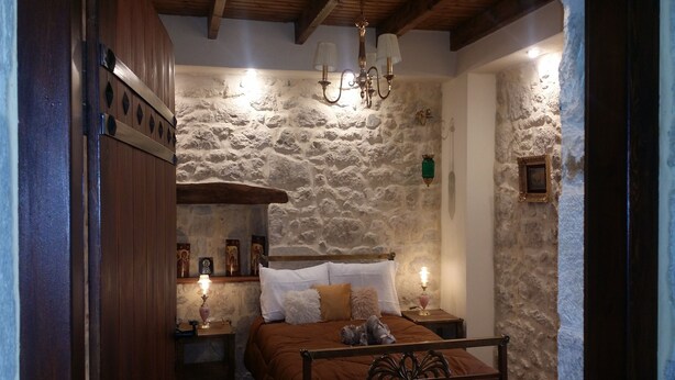 A cozy bedroom with a stone wall, a wooden bed frame, and a nightstand with a lamp. - Amazing Stone villa (Gortyna)