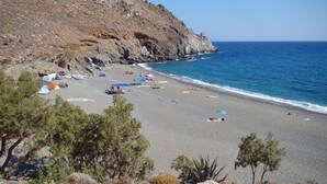A beach with tents and umbrellas, rocky cliffs, and a clear blue sea. - Amazing Stone villa (Gortyna)