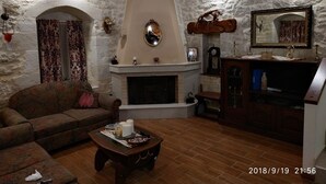 A cozy living room with a fireplace, a sofa, a coffee table, and a wooden cabinet. - Amazing Stone villa (Gortyna)