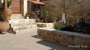 A stone-walled courtyard with steps leading to a wooden gate, potted plants, and a water feature. - Amazing Stone villa (Gortyna)
