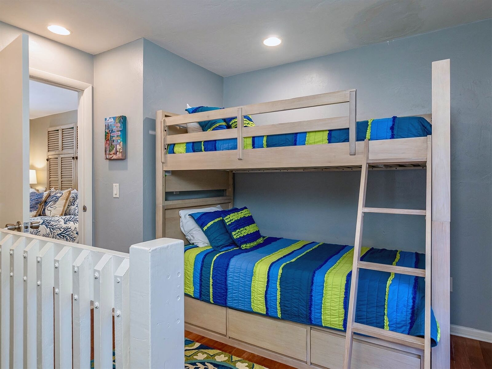 A bunk bed with blue and green bedding, a white railing, and a small rug on the floor.