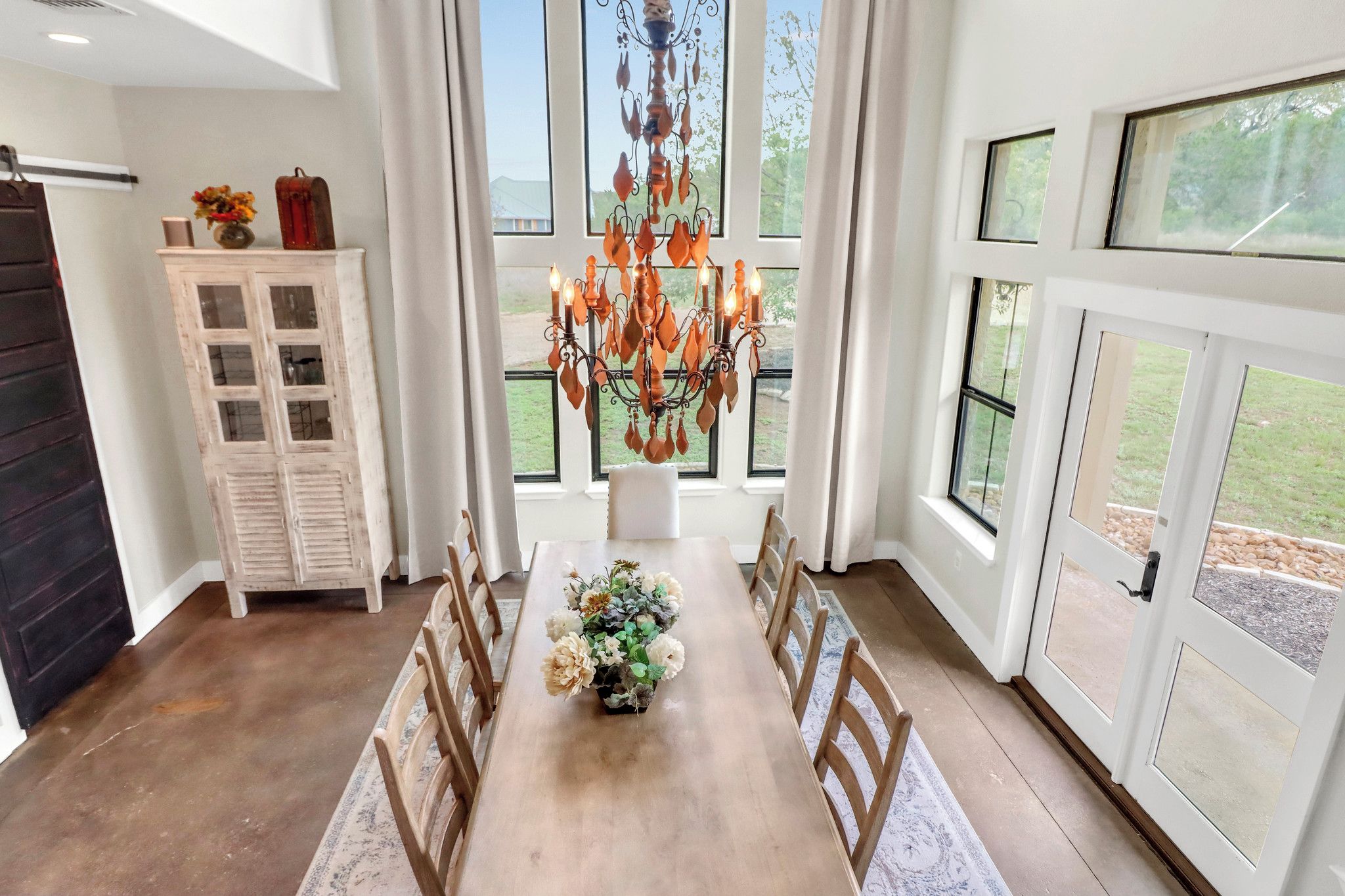 Un coin repas avec une table en bois, des chaises, un lustre et un buffet orné de fleurs.