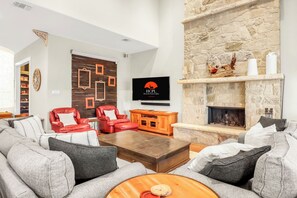 Una sala de estar con chimenea de piedra, sillones de cuero rojo, un sofá gris y un televisor de pantalla plana montado en la pared.