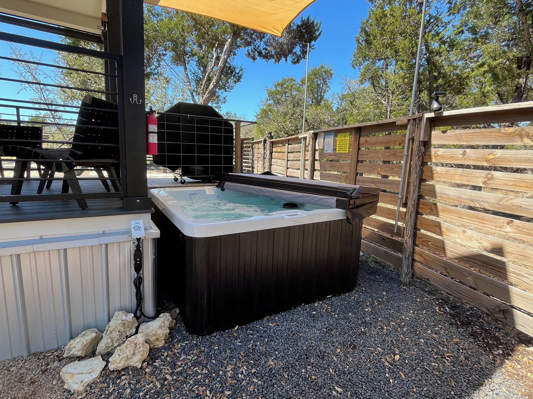Ein Whirlpool mit Holzterrasse, Grill und Holzzaun.