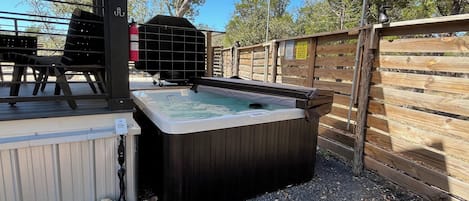 Ein Whirlpool mit Holzterrasse, Grill und Holzzaun.