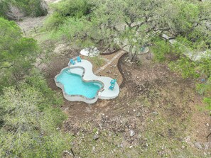 Vista aérea de una piscina de forma inusual, rodeada de jardines con árboles y arbustos.
