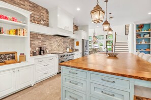 Una cocina con armarios blancos, una isla de madera, un rebozo de ladrillo y lámparas colgantes.