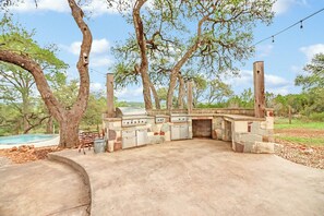 An outdoor barbecue area with stone-built grill stations, a concrete seating area, and a pool in the background. - 4BR Canyon Lake Retreat with New Private Pool & Outdoor Living (Canyon Lake)