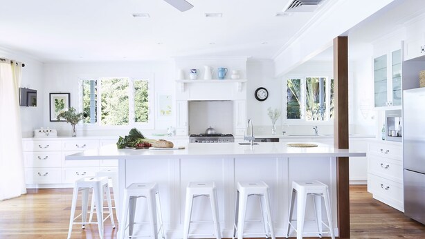 A modern kitchen with white cabinetry, a central island with stools, a stove, and a large window providing natural light.