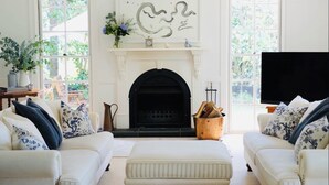 A living room with a fireplace, two white sofas with floral cushions, a coffee table, and a TV on the right.