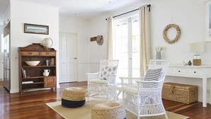 A bright, white-walled room with a wooden floor, a white desk, wicker chairs, a globe, and a bookshelf.