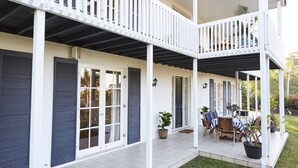 A two-story house with a covered patio area, featuring a dining set and potted plants.