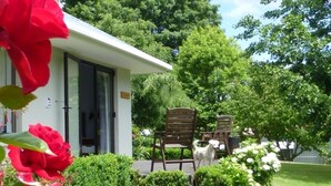 A house with a patio area featuring two wooden chairs and a small white dog. - Tasteful spacious private garden quest house (Katikati)
