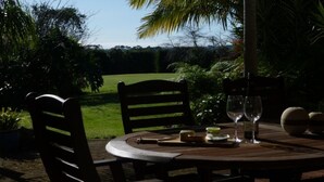 A round wooden table with two chairs, a bottle, a glass, and a small plate with a piece of cheese. - Tasteful spacious private garden quest house (Katikati)