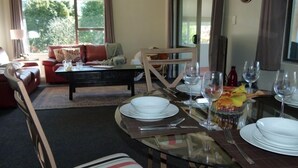 A dining area with a glass table set for four, surrounded by a cozy living room with a sofa and a coffee table. - Tasteful spacious private garden quest house (Katikati)