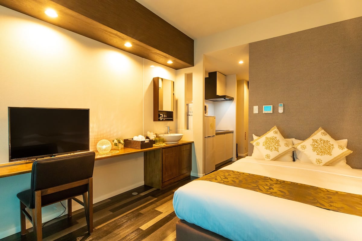 A hotel room with a bed, a desk with a chair, a TV, a sink, and a mirror.