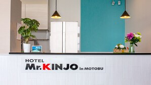 A hotel reception desk with a sign reading "HOTEL Mr. KINJO in MOTOBU". There are two pendant lights, a potted plant, and a vase with flowers on the counter. - Mr.KINJO in MOTOBU OCEAN TERRACE (Motobu)
