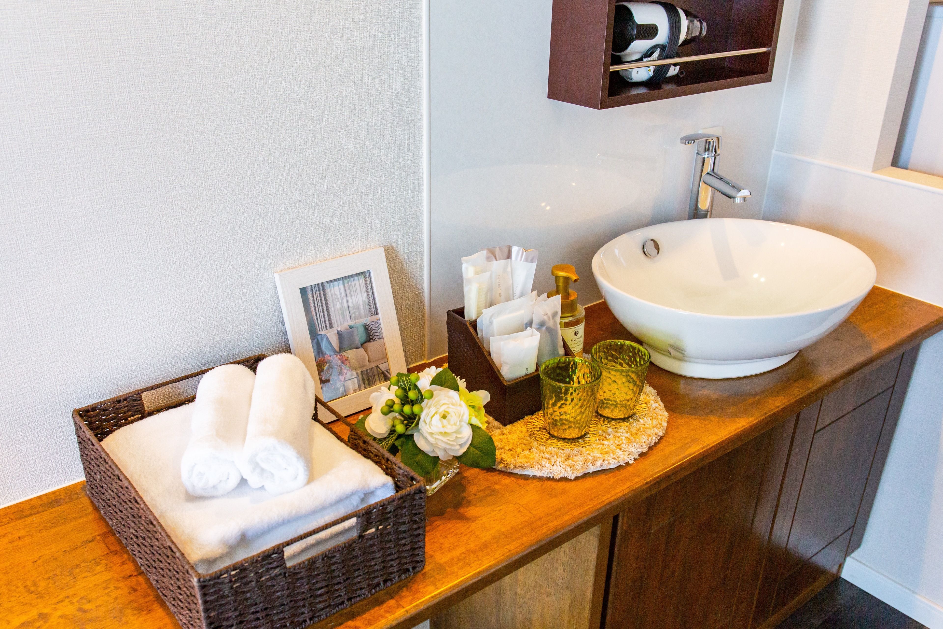A bathroom with a white sink, a framed photo, a basket of towels, and toiletries on the counter.