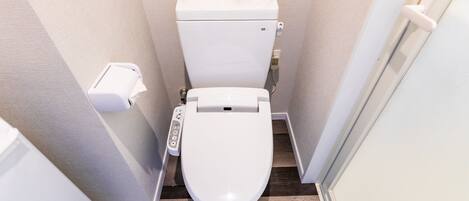 Een kleine, moderne badkamer met een wit toilet, een handdroger en een papieren handdoekdispenser.
