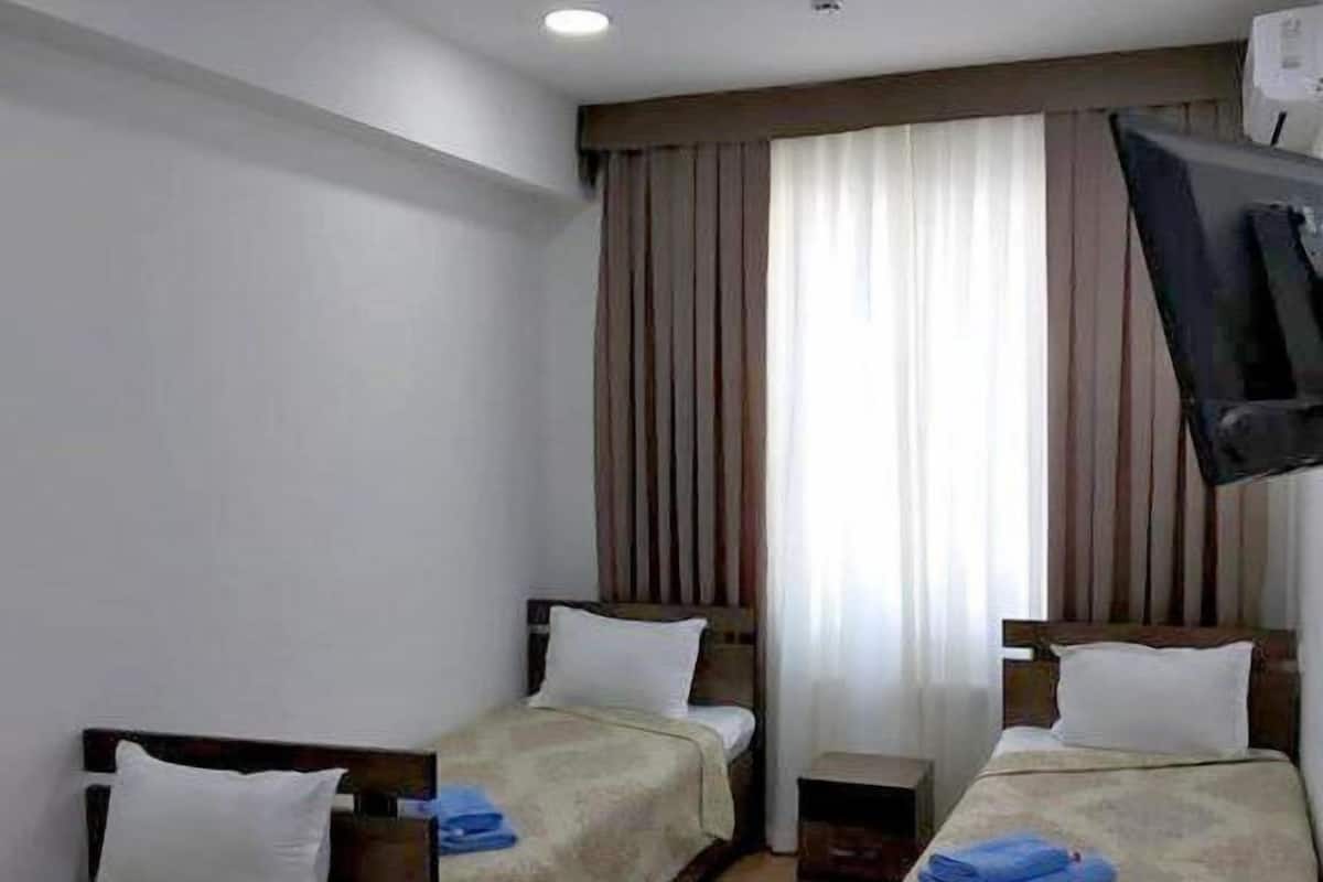 Une chambre d’hôtel avec deux lits simples, un téléviseur fixé au mur et une fenêtre avec des rideaux.