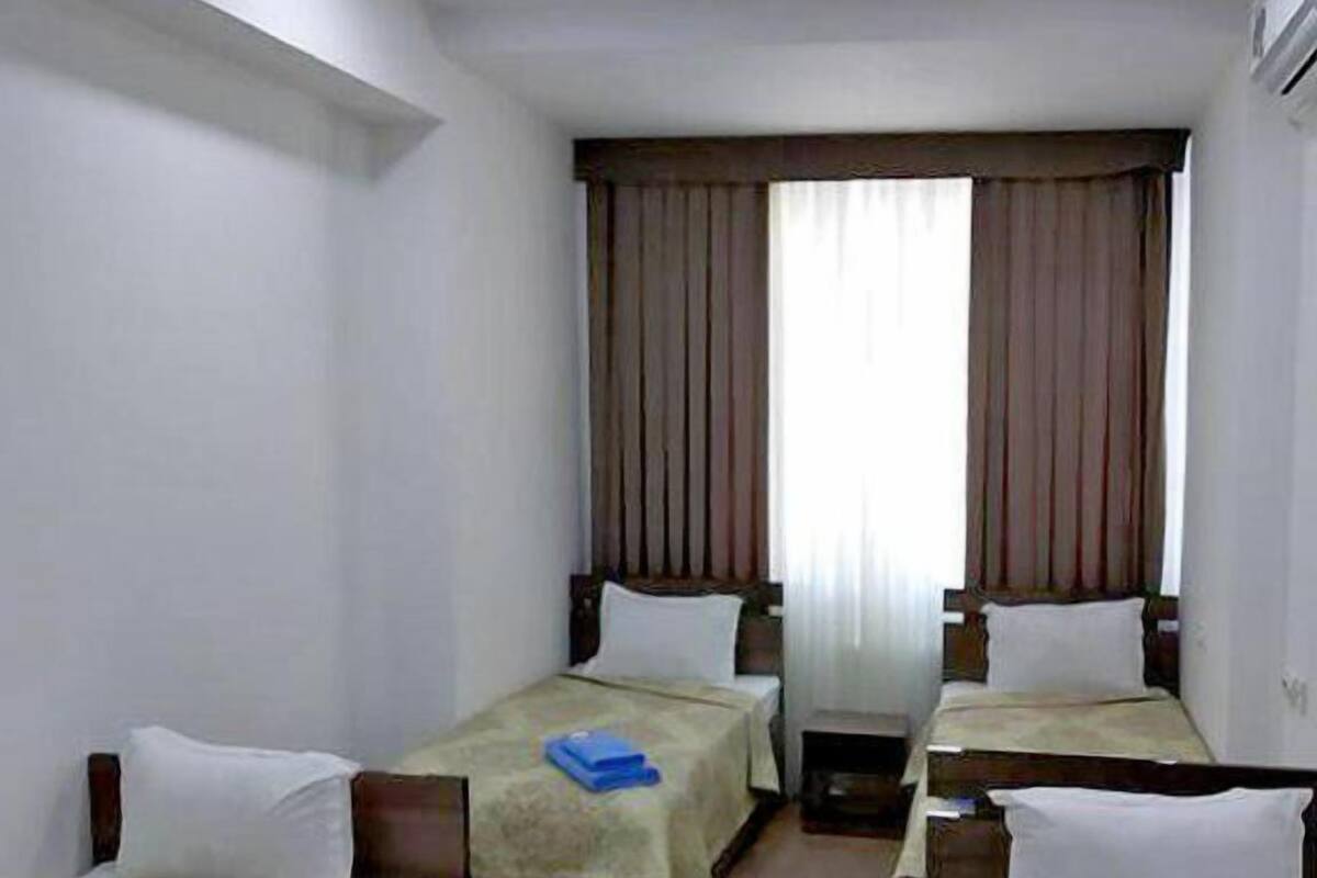 Une chambre d’hôtel avec trois lits simples, une grande fenêtre avec des rideaux et un luminaire au plafond.