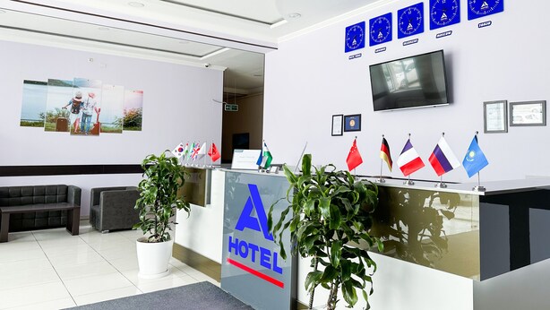 A hotel reception area with a modern design, featuring a reception desk, seating area, and a wall with clocks and flags. - Magistral (Urtaaul)
