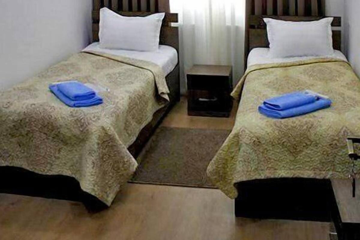 Une chambre d’hôtel avec deux lits simples, une petite table et une fenêtre avec des rideaux.