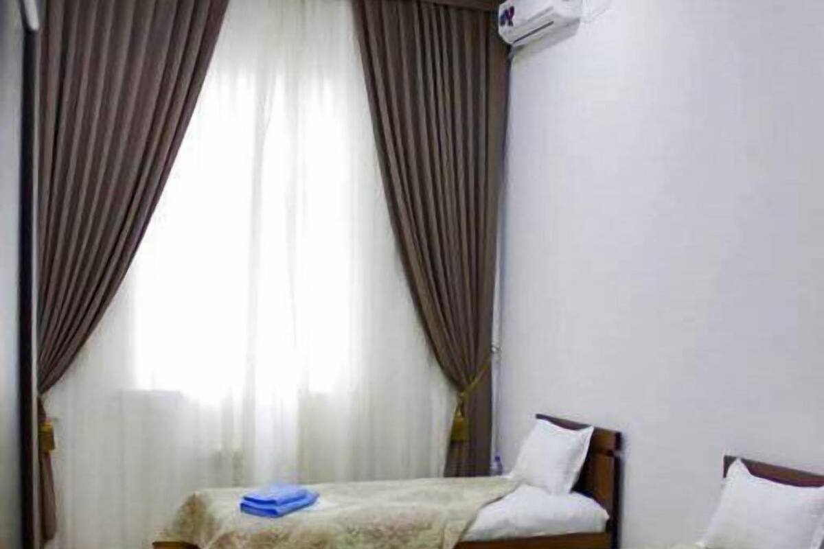 Une chambre d’hôtel avec deux lits simples, une fenêtre avec des rideaux, un appareil de climatisation et un plancher en bois.