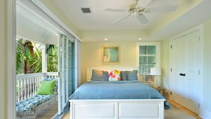A bedroom with a large bed, a ceiling fan, a window with blinds, a bedside table with a lamp, and a view of the outdoors. - Luxury 3-Bedroom Waterfront Home with Pool AND Dock! (Key West)