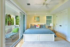 A bedroom with a large bed, a ceiling fan, a window with blinds, a bedside table with a lamp, and a view of the outdoors. - Luxury 3-Bedroom Waterfront Home with Pool AND Dock! (Key West)