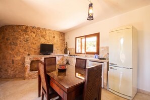 A kitchen with a stone wall, a dining table with chairs, a television, and a refrigerator.