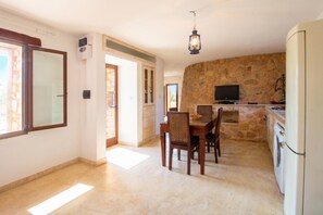 A kitchen with stone walls, a dining area with chairs, a TV, and a washing machine.