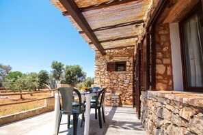 A stone building with a balcony, outdoor seating, and a view of trees.