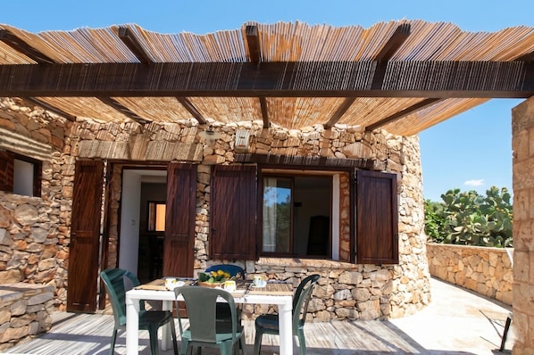 A stone building with a covered patio, wooden shutters, and a table with chairs.