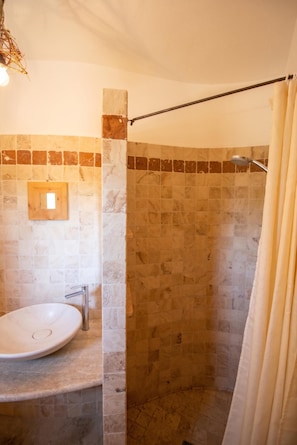 Ein Badezimmer mit einer Dusche aus Steinplatten, einem Waschbecken mit Marmorplatte und einem spiegelnden Wandspiegel mit Holzrahmen.