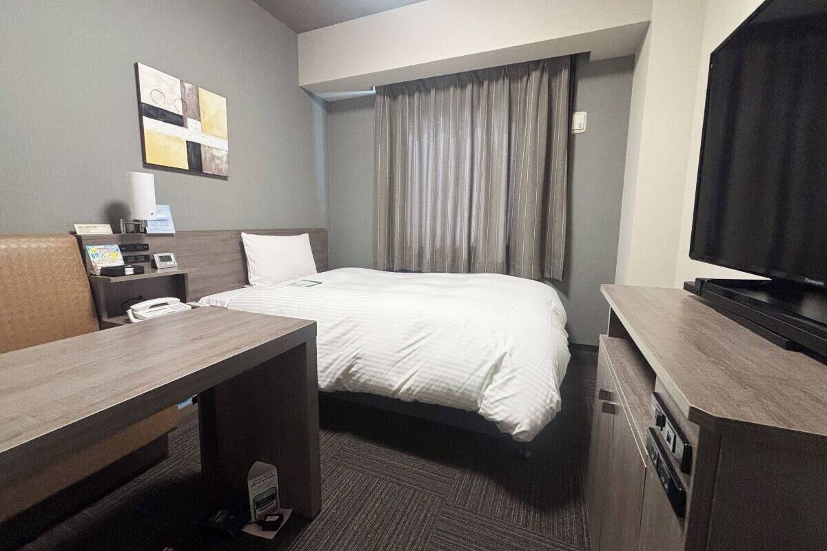 Ein Hotelzimmer mit Bett, Schreibtisch, Fernseher und Telefon.