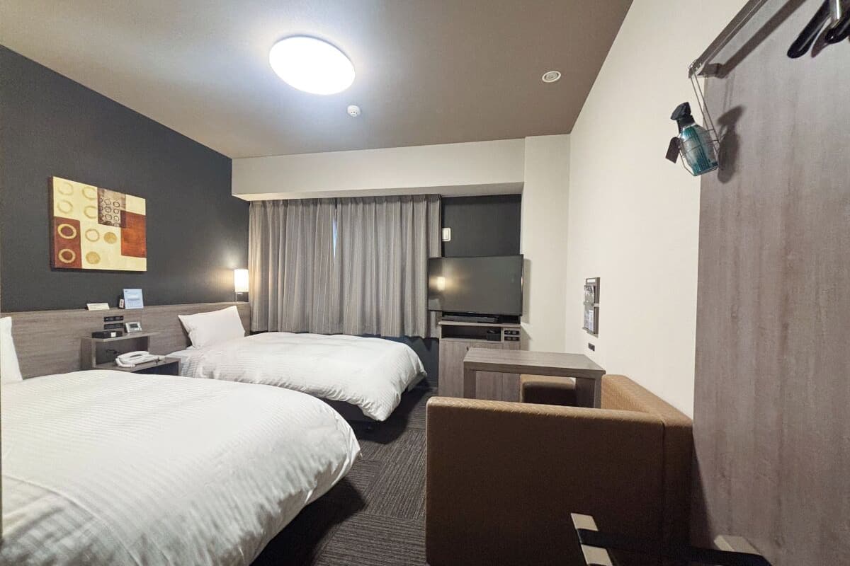 Ein Hotelzimmer mit zwei Betten, einem Schreibtisch, einem Stuhl, einem Fernseher und einem Badezimmer mit Duschvorhang.