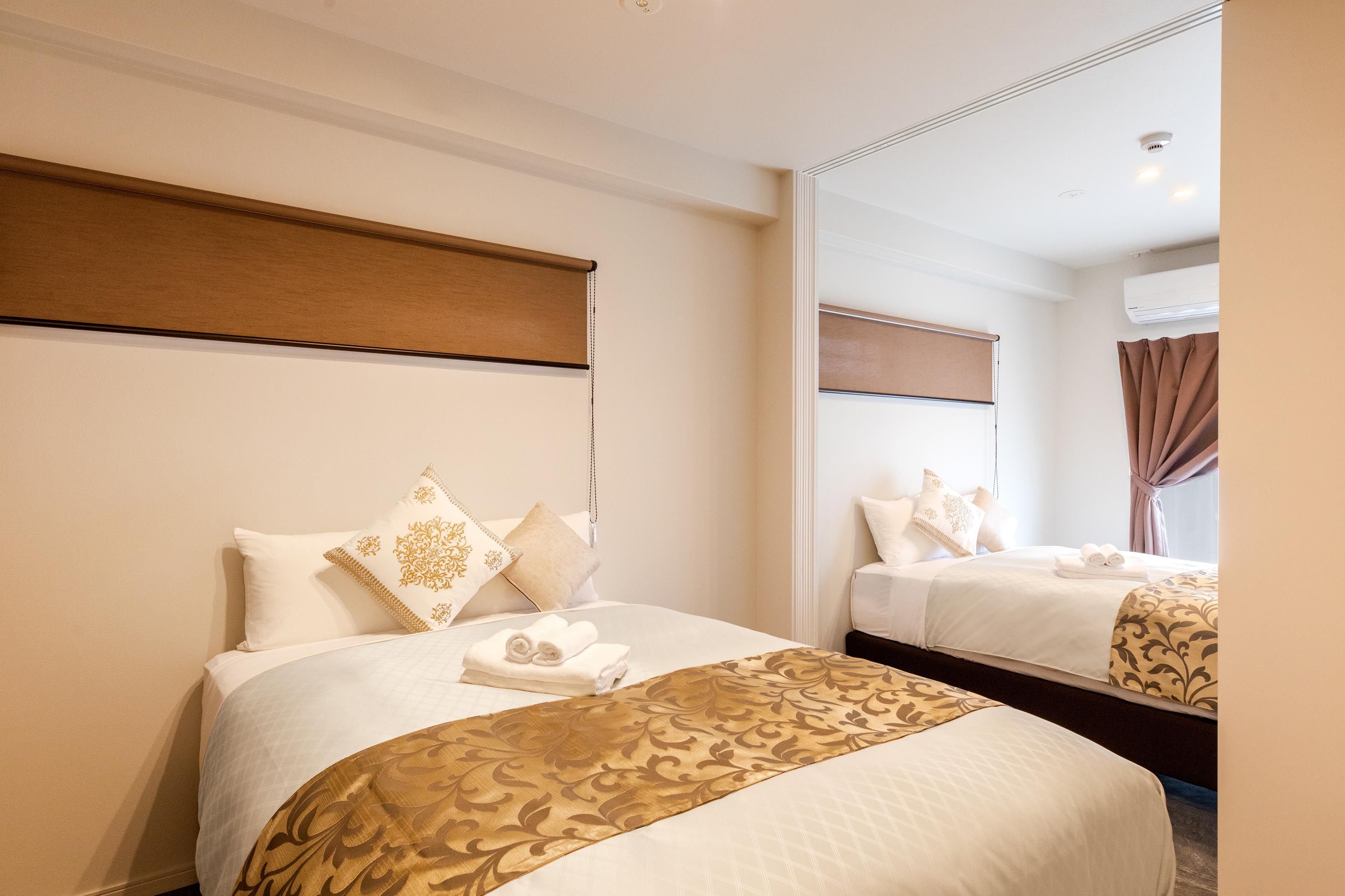 Habitación de hotel con dos camas, cada una con cabecero, un espejo grande y una ventana con cortinas.