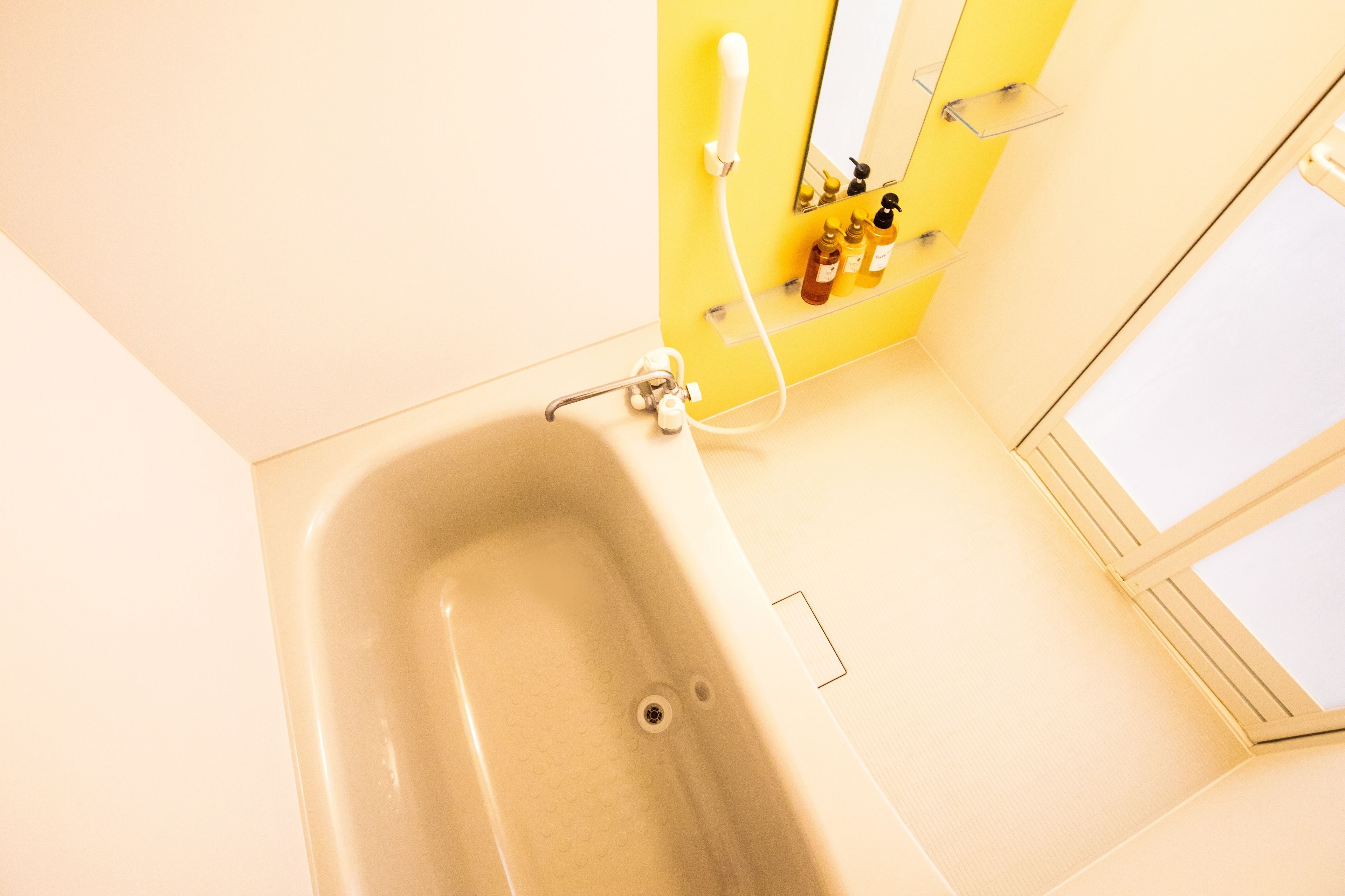 A bathroom with a bathtub, a yellow wall, and a window.