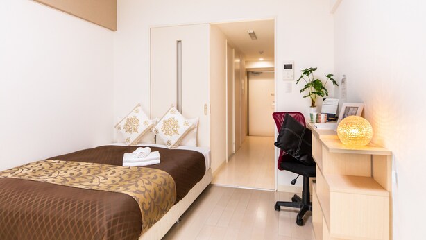 A hotel room with a bed, a desk with a lamp, a chair, and a plant. - Mr.KINJO PREMIUMHOME in CHATAN 2 (Chatan)