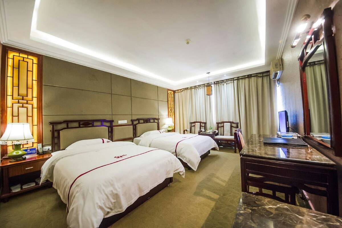 A hotel room with two beds, a desk, a chair, a lamp, and a mirror.