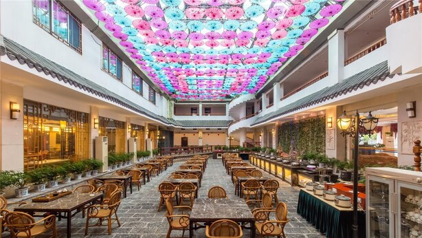 Un vaste espace intérieur aménagé en salle à manger, avec de nombreuses tables et chaises, un plafond décoré de parasols colorés et un style architectural traditionnel.