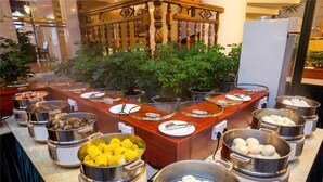 Un buffet composé de différents plats présentés dans des récipients en acier inoxydable, avec un comptoir en bois et un escalier en arrière-plan.