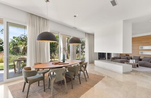 Un salon moderne avec un grand canapé, un coin repas doté d’une table ronde et de chaises, et une cuisine avec un comptoir blanc.