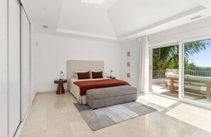 Une chambre à coucher moderne avec un grand lit, une table de chevet, un banc et une vue sur l’extérieur.