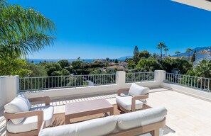 A terrace with outdoor furniture, a view of the sea, and surrounding greenery. - Villa near Beach with Pool & Panoramic Views (Marbella)