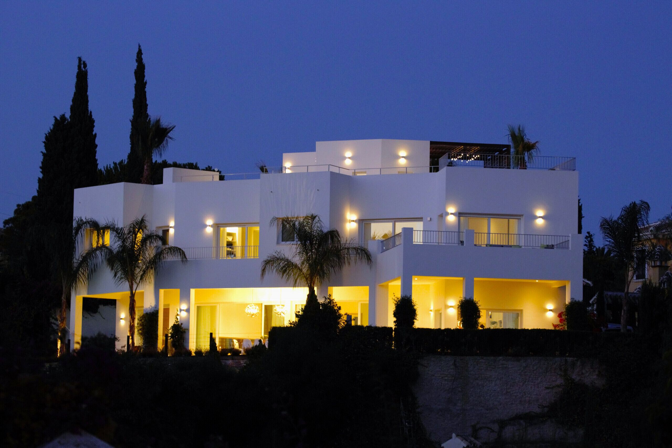 A modern multi-story house with multiple balconies and illuminated windows.