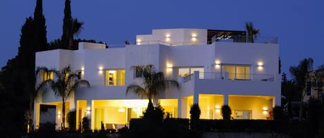 A modern multi-story house with multiple balconies and illuminated windows.