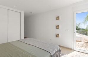 Et soveværelse med seng, skydedør, balkon med gelænder og tre billeder i rammer på væggen.