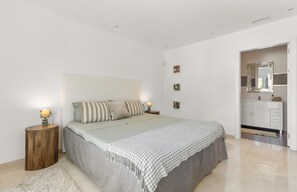 Une chambre à coucher comprenant un lit, des tables de chevet, une commode, un miroir et une salle de bain visible à travers une porte ouverte.